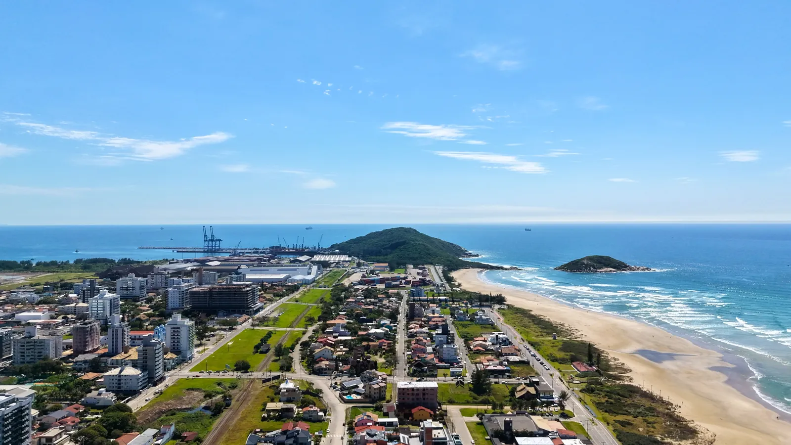 Vista aérea da orla, com a praia, o morro e o porto ao fundo.